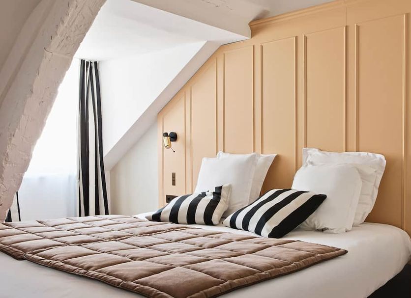 New Hotel Lafayette Paris bedroom with sloped ceiling, beige paneled wall, and striped pillows on bed