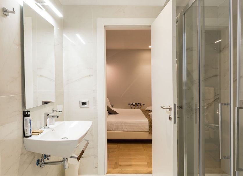 Floris Hotel Rome bathroom with glass shower, sink, and view into a bedroom