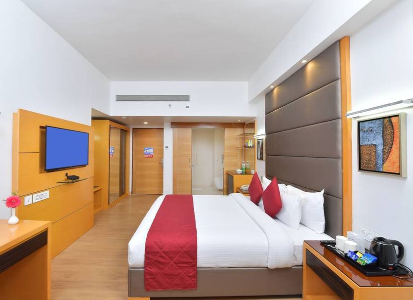 The Central Residency, Thiruvananthapuram guest room with king bed, wall-mounted TV and wooden accents