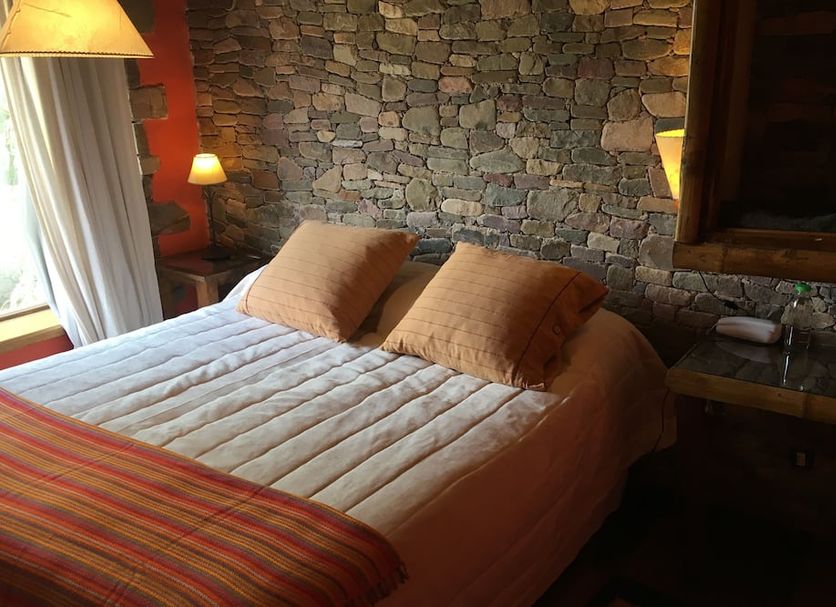 Refugio Del Pintor in Tilcara guest room with stone wall, double bed and warm bedside lamps