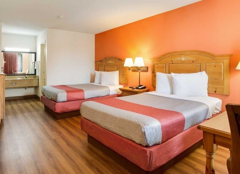 Motel 6 Clarksville Tn guest room with two beds, orange accent wall, and vanity area in Clarksville
