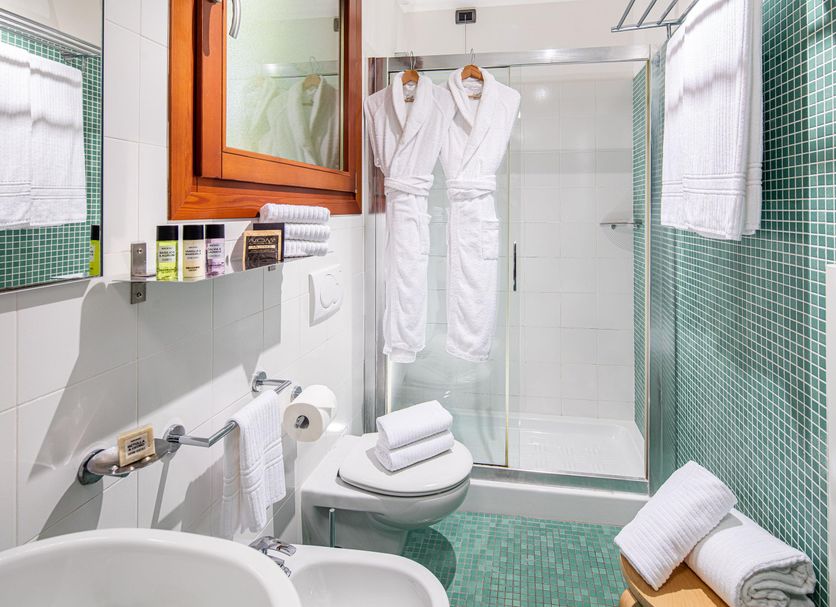 Hotel La Pergola bathroom in Lignano Sabbiadoro with shower, towels, robes and green tile