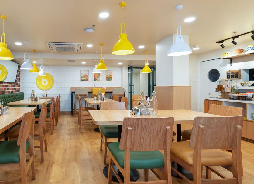 Bloom Hotel - Sg Highway, Ahmedabad dining area with wooden tables, green seating and yellow pendant lights