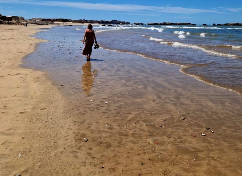 Dar Nafoura-Mogador in Essaouira: beach with person walking along the shoreline and ocean waves