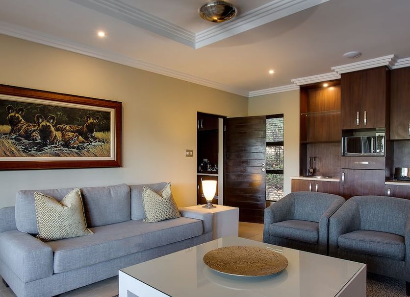 Shepherd's Tree Game Lodge in Pilanesberg living room with gray sofa, chairs, and kitchenette