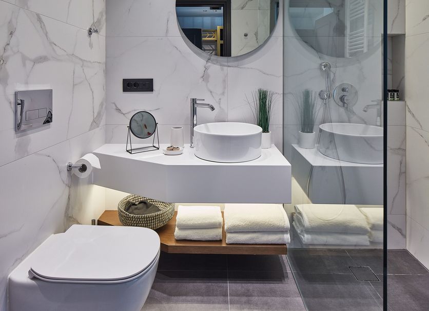 Lithia Boutique Hotel in Ioánnina bathroom with marble-look walls, round mirrors, vessel sink and glass shower
