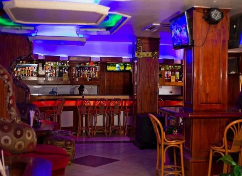 The Tick Hotel Kampala bar and lounge with colorful lighting, stools, and wall-mounted TV