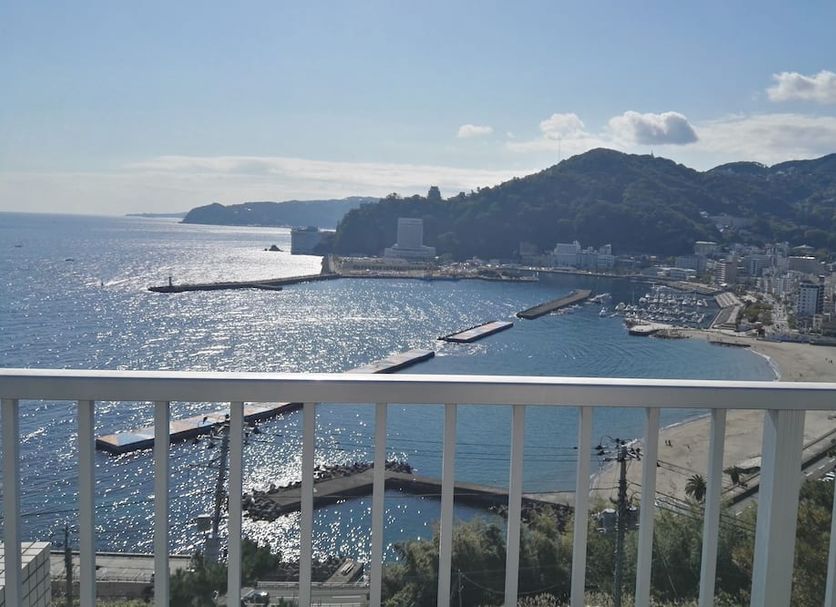 Atami Onsen Guest House Megumi in Atami with a balcony view of the bay, beach, and mountains