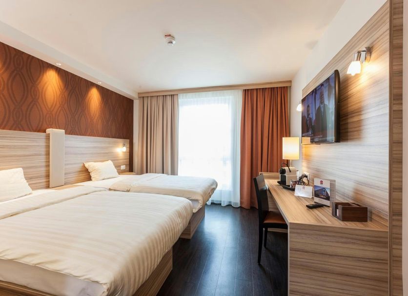 Staycity Aparthotels Heidelberg room with two beds, desk, wall-mounted TV and window light