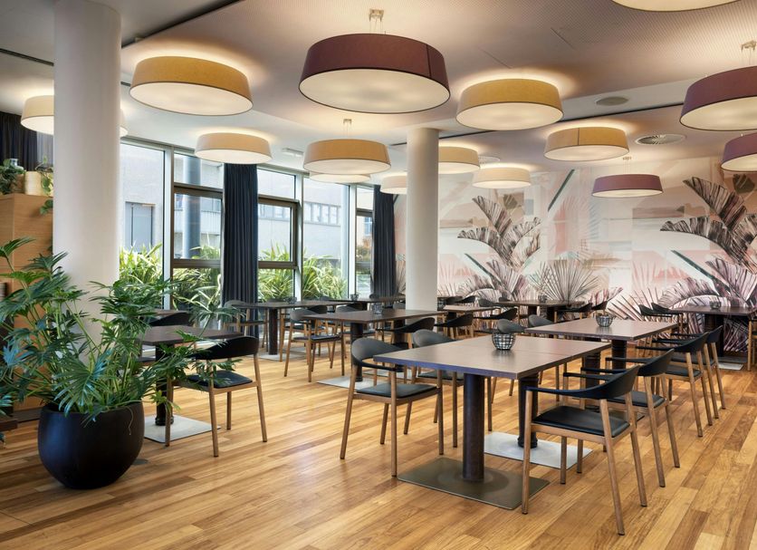 Four Points by Sheraton Bolzano dining area with large windows, tables, chairs, and potted plants