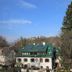 Haus Wartenberg in Salzburg with a green-roofed hotel building beside tall trees under a blue sky.