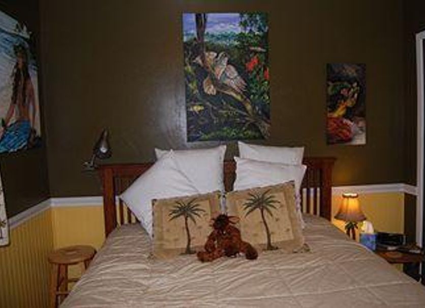 The Artist Cottage - Bed And Breakfast in Volcano: cozy bed with palm tree pillows and tropical wall art