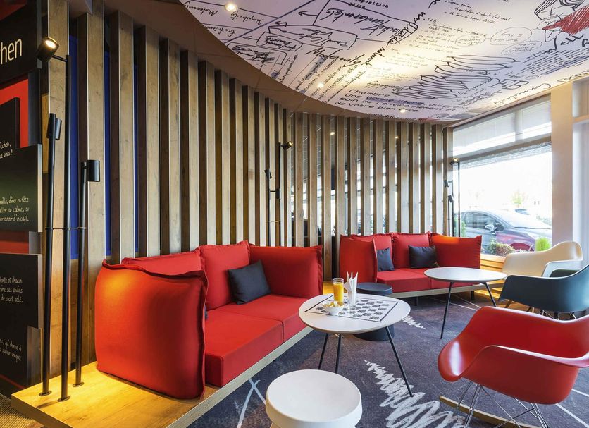 Ibis Deauville Centre lobby lounge with red sofas, modern chairs and large front window in Deauville