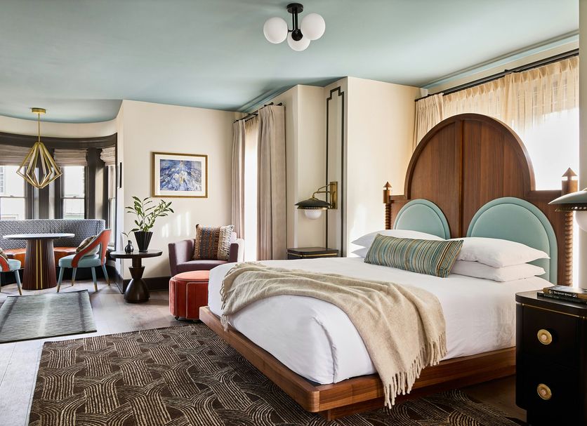 Zelda Dearest in Asheville, bedroom with arched wood headboard, teal chairs, and dining area