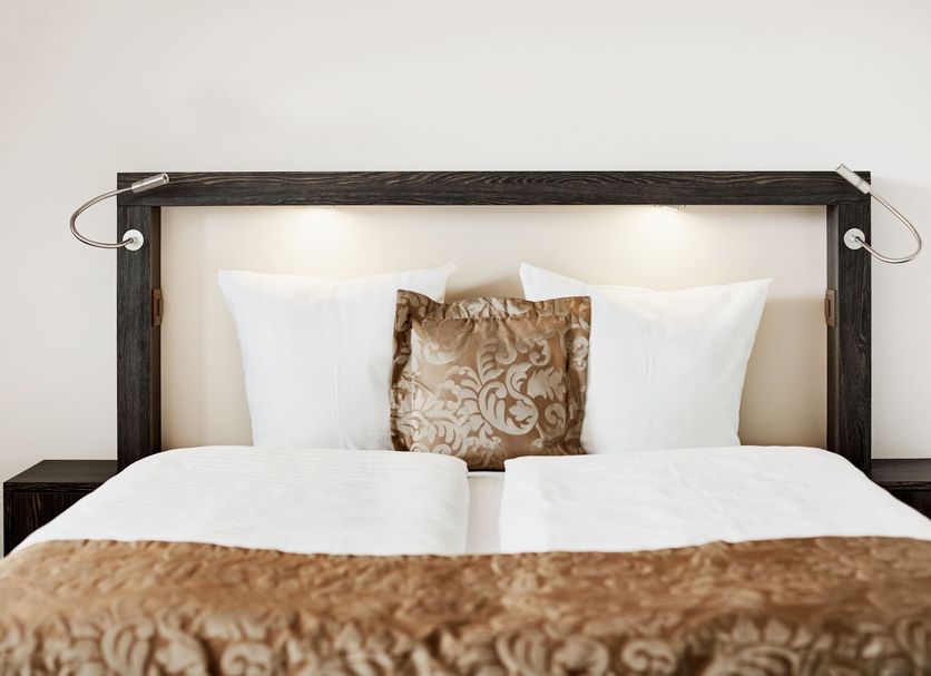 Hotel Schäfli in Uzwil bedroom with neatly made bed, white pillows and brown patterned accent cushion