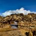 Beach Hotel Jacuma in João Pessoa with a rocky natural arch on the shoreline under a blue sky.