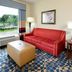Hampton Inn & Suites Durham/North I-85 guest room with red sofa, ottoman and window view in Durham