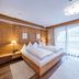Hotel Englhof in Zell am Ziller bedroom with wooden bed, bedside lamps and balcony door with sheer curtains
