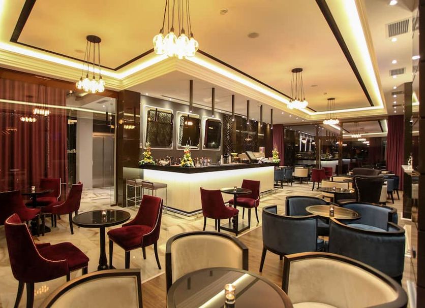 Senator Hotel Tirana lounge bar with red velvet chairs, marble tables and warm ceiling lighting