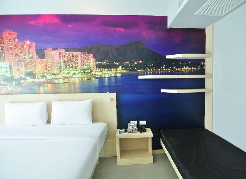 The Aim Patong Hotel room with bed, bench, and wall mural of Patong bay skyline