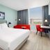 Hyatt Place London City East guest room with king bed, red sofa, desk and city view in London