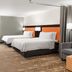 Home2 Suites by Hilton Alexandria guest room with two beds, sofa, floor lamp and colorful wall art