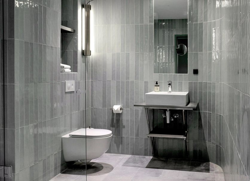 Boutique Hotel Hans Copenhagen bathroom with wall-mounted toilet, sink vanity and gray tile shower area