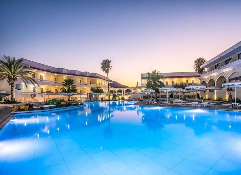 Niriides Beach in Kolympia with a lit outdoor pool and palm trees at dusk