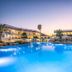 Niriides Beach in Kolympia with a lit outdoor pool and palm trees at dusk