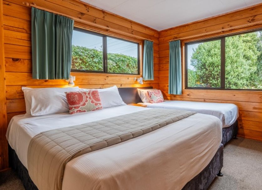 Tasman Holiday Parks - Coromandel cabin bedroom with two beds and large windows overlooking trees