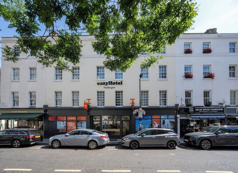 Easyhotel Paddington in London with white facade, street-level entrance, parked cars and tree shade