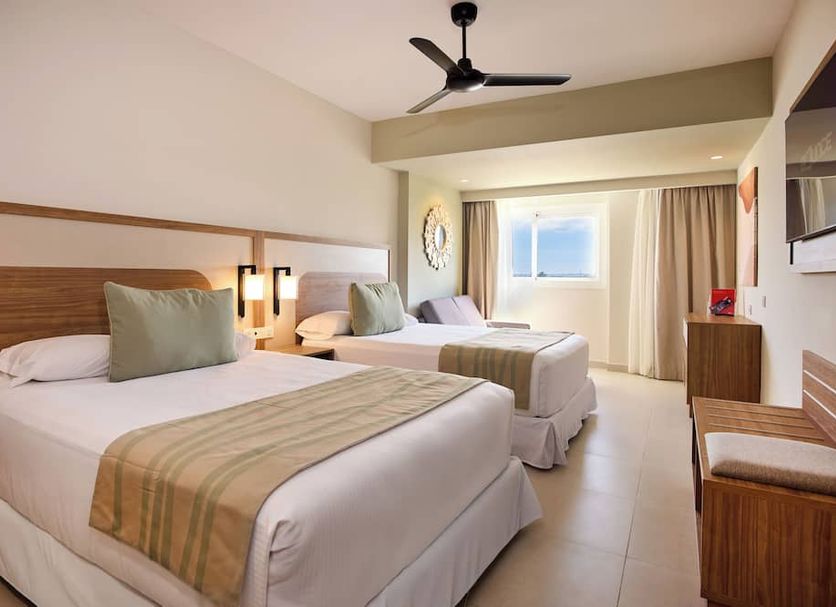 Hotel Riu Negril in Negril: bright guest room with two beds, ceiling fan, and window view