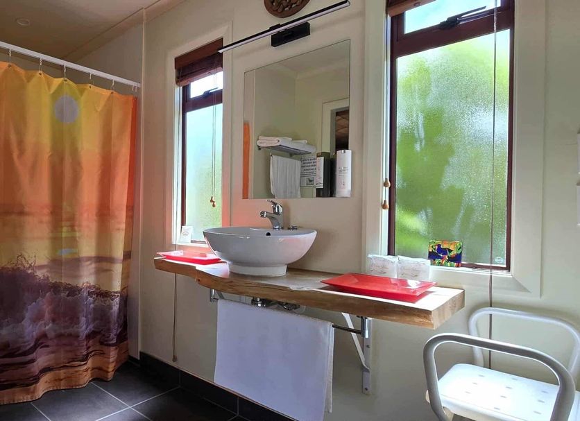 The Rocks Chalets, Takaka: bright bathroom with shower, vanity sink, towel rack and chair