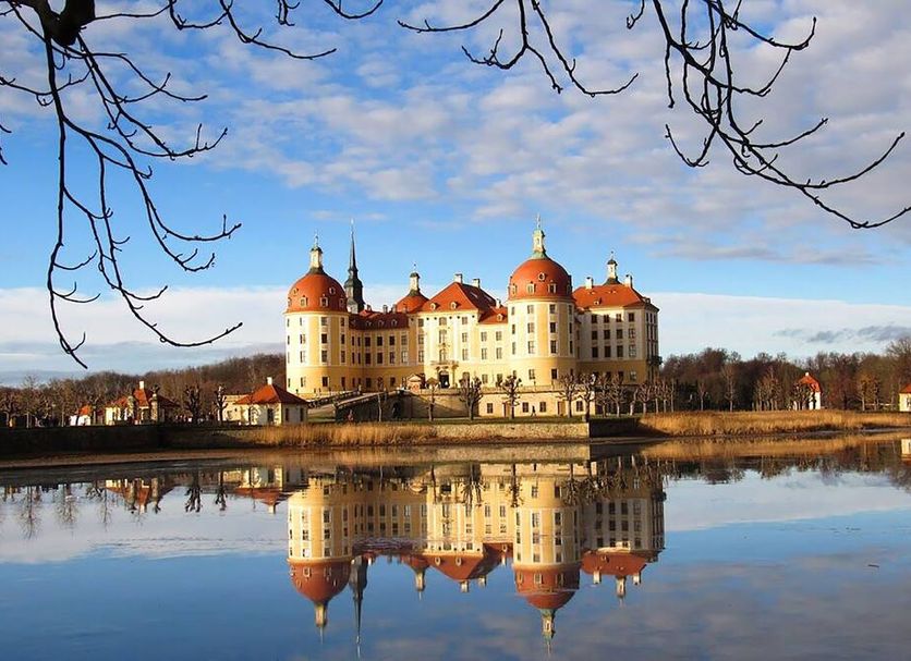 City Hotel Dresden Radebeul in Radebeul reflected in a calm lake beside a castle-like building