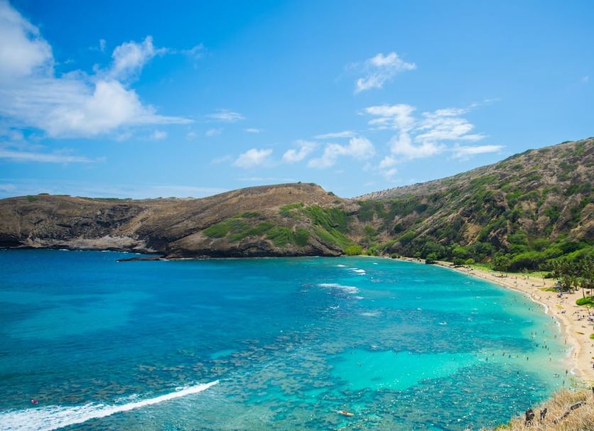 White Sands Hotel in Honolulu with a turquoise tropical bay, sandy beach, and green hillside