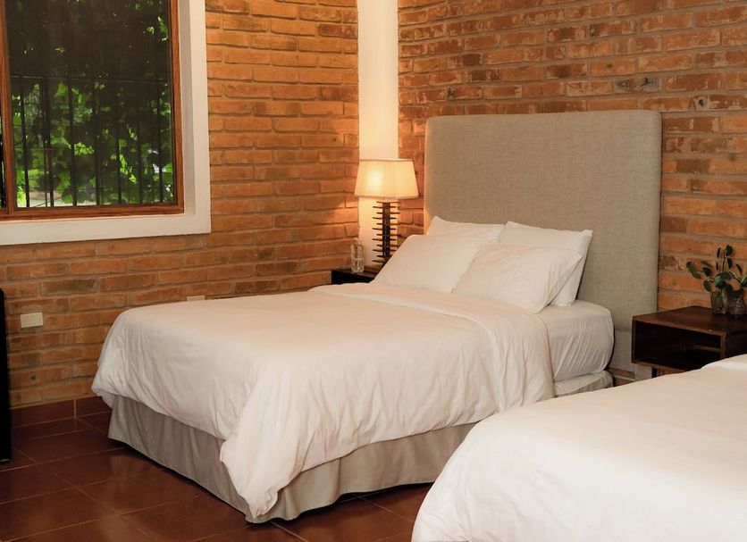 Caracoral Hotel Boutique in El Valle de Anton bedroom with two white beds, brick walls and bedside lamp