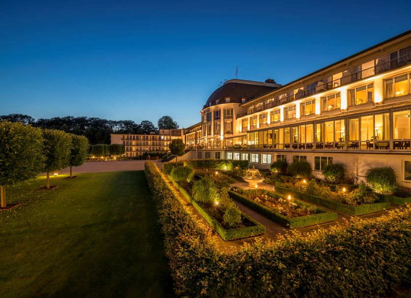 Parkhotel Bremen Hommage in Bremen at dusk, with lit terraces, manicured gardens and lawn