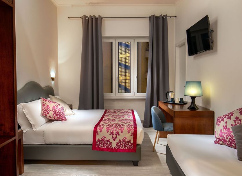 Prima Guest House Collection in Rome guest room with twin beds, desk, wall-mounted TV and window curtains