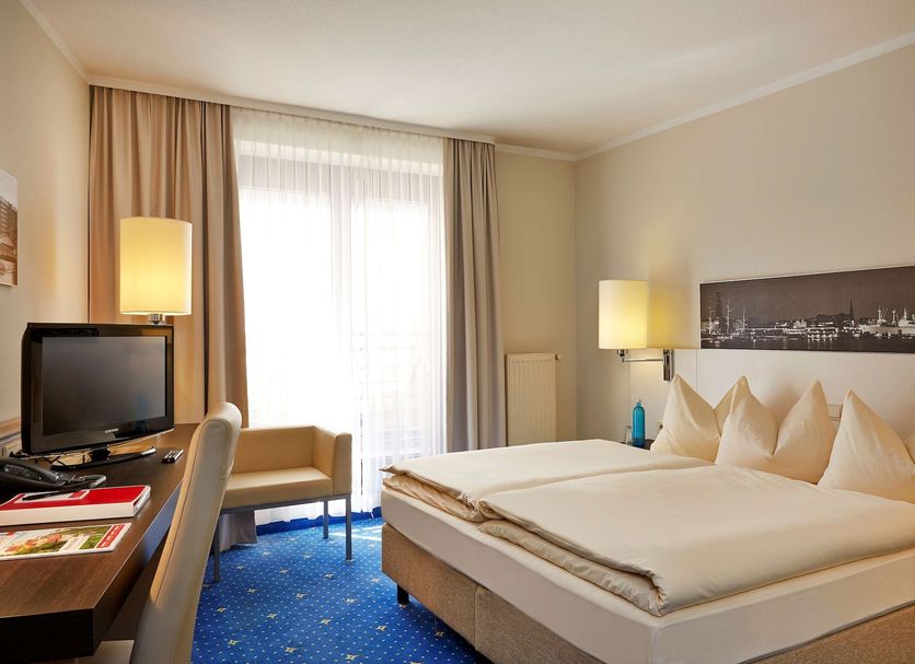 H4 Hotel Hamburg Bergedorf guest room with double bed, desk, TV and large window in Hamburg