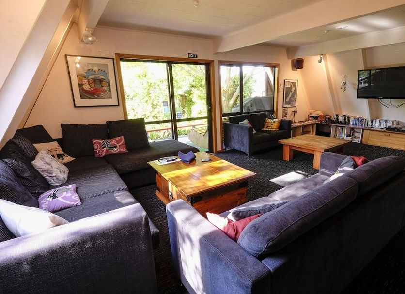 Haka Lodge Christchurch lounge with sofas, coffee table, TV, and sliding doors to a balcony