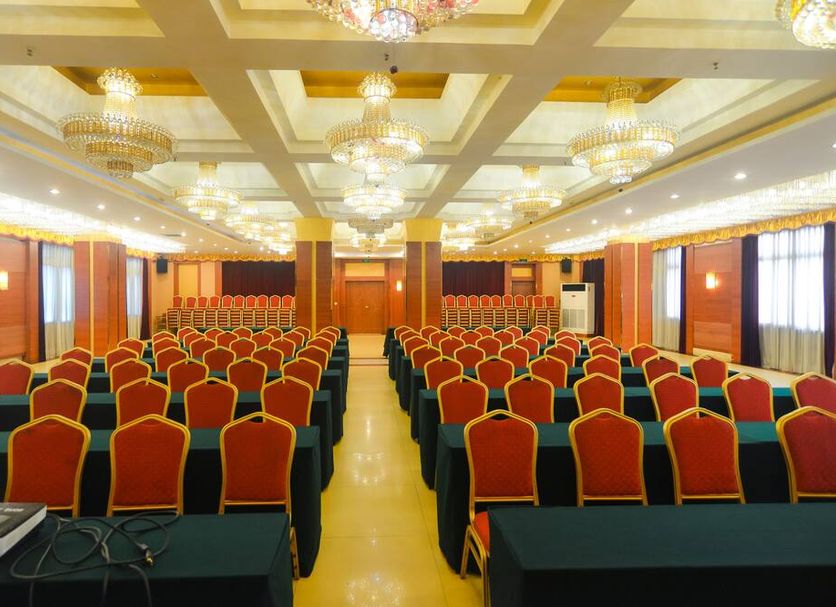Qinhuangdao Yang Cheng Hotel in Qinhuangdao conference hall with rows of red chairs and chandeliers