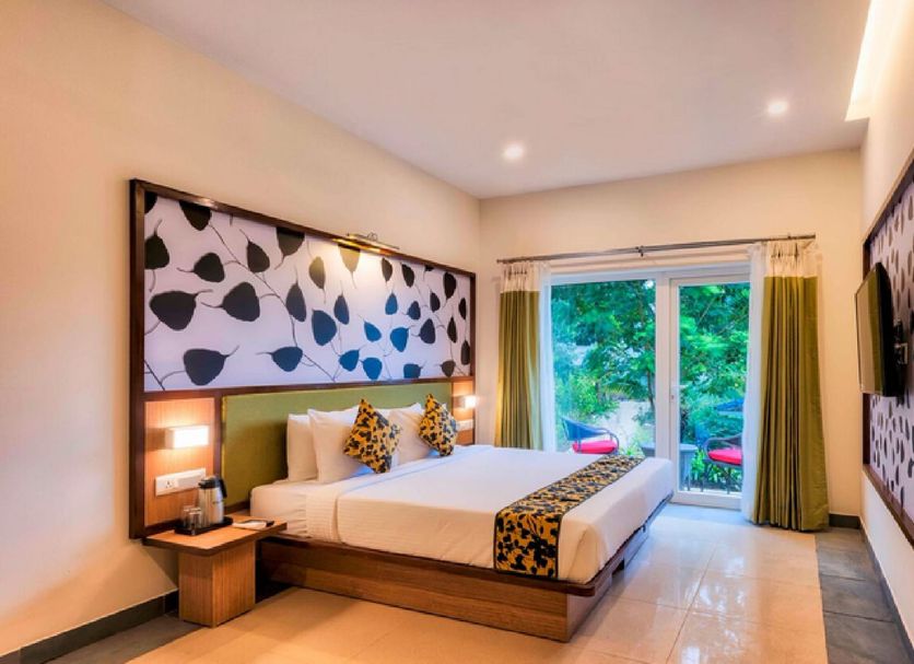 Sterling Wayanad in Sultan Bathery bedroom with king bed, leafy wall art and sliding glass doors to greenery