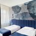Szydlowski Gdansk guest room with two single beds, blue upholstered headboard and leaf mural wall