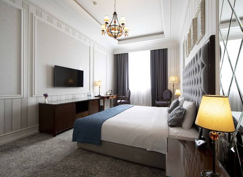 Sapphire City Hotel Baku guest room with king bed, chandelier, and wall-mounted TV