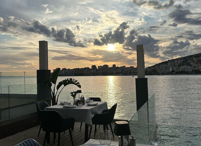 Demi Hotel, Sarandë: seaside dining terrace with table setting and sunset view over the water