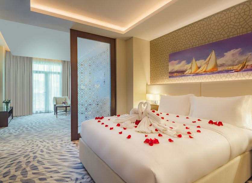 Riviera Rayhaan by Rotana Doha guest room with rose-petal bed decor and seating area
