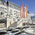 Grand Hotel Zell am See in Zell am See with snowy gardens, flags, and a fountain before mountain views