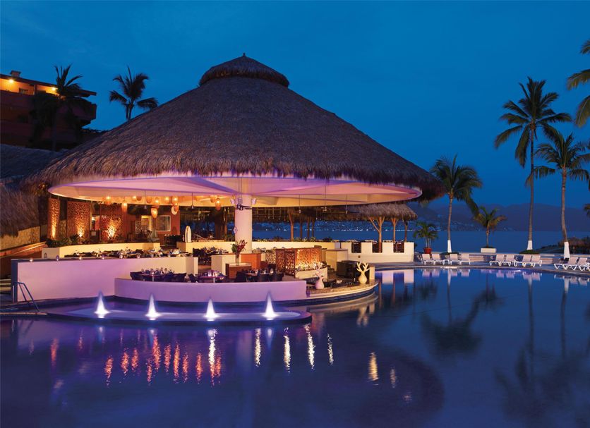 Sunscape Puerto Vallarta Resort & Spa poolside thatched palapa bar at night with palm trees and ocean view