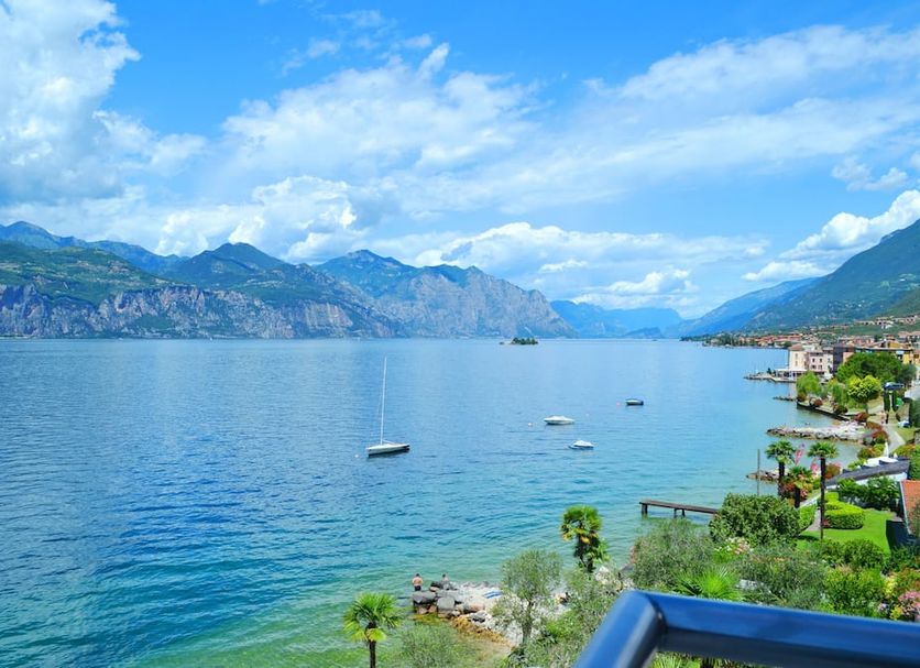 Belfiore Park Hotel in Brenzone with lake view, mountains, and a lush shoreline by clear blue water.