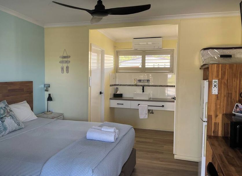 Moore Park Beach Inn room in Bargara with bed, kitchenette, ceiling fan and wood furnishings